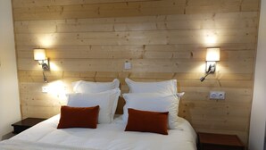 A hotel room with a wooden headboard, two bedside tables, a bed with white bedding and two orange pillows, and wall-mounted reading lamps.