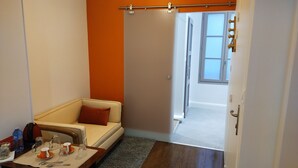 A small, cozy room with a sofa, a table set with cups and a bottle, and a door leading to another room.