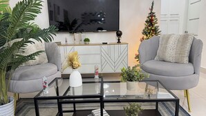 Un salon moderne avec une table basse en verre, deux canapés gris, un téléviseur fixé au mur et un sapin de Noël.