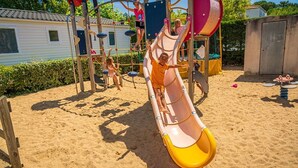 A playground with a slide, climbing structures, and a sandy ground. - ZEcamping 4 étoiles 200m plage piscine couverte club enfant mobil-home TV (La Faute-sur-Mer)