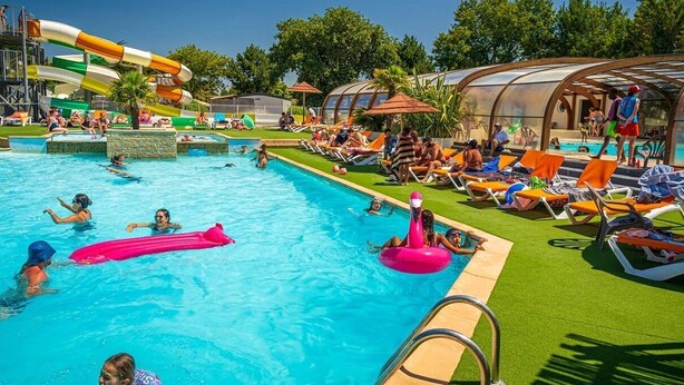 A swimming pool area with multiple pools, lounge chairs, and a water slide. - ZEcamping 4 étoiles club enfant parc aquatique sauna hammam chiens acceptés (Saint-Georges-d'Oléron)