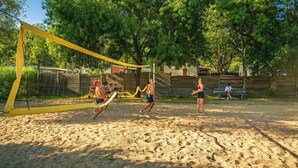 A sandy beach volleyball court with a yellow net, surrounded by trees and a wooden fence. - ZEcamping 4 étoiles club enfant parc aquatique sauna hammam chiens acceptés (Saint-Georges-d'Oléron)