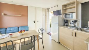 A compact kitchenette with a microwave, coffee maker, and sink. There is a dining area with a table and chairs, and a blue sofa. - ZEcamping 4 étoiles club enfant parc aquatique sauna hammam chiens acceptés (Saint-Georges-d'Oléron)