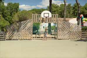 Guests can enjoy a game of basketball on the outdoor court, surrounded by trees and a clear sky.