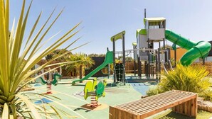 Une aire de jeux avec un toboggan, des structures d’escalade et un banc en bois.