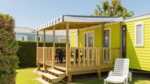 Une maison mobile jaune avec une terrasse en bois et un patio couvert.