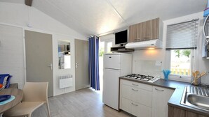 A compact kitchen with a gas stove, a built-in oven, and a microwave. There is a dining area with a table and chairs, and a window with blinds.