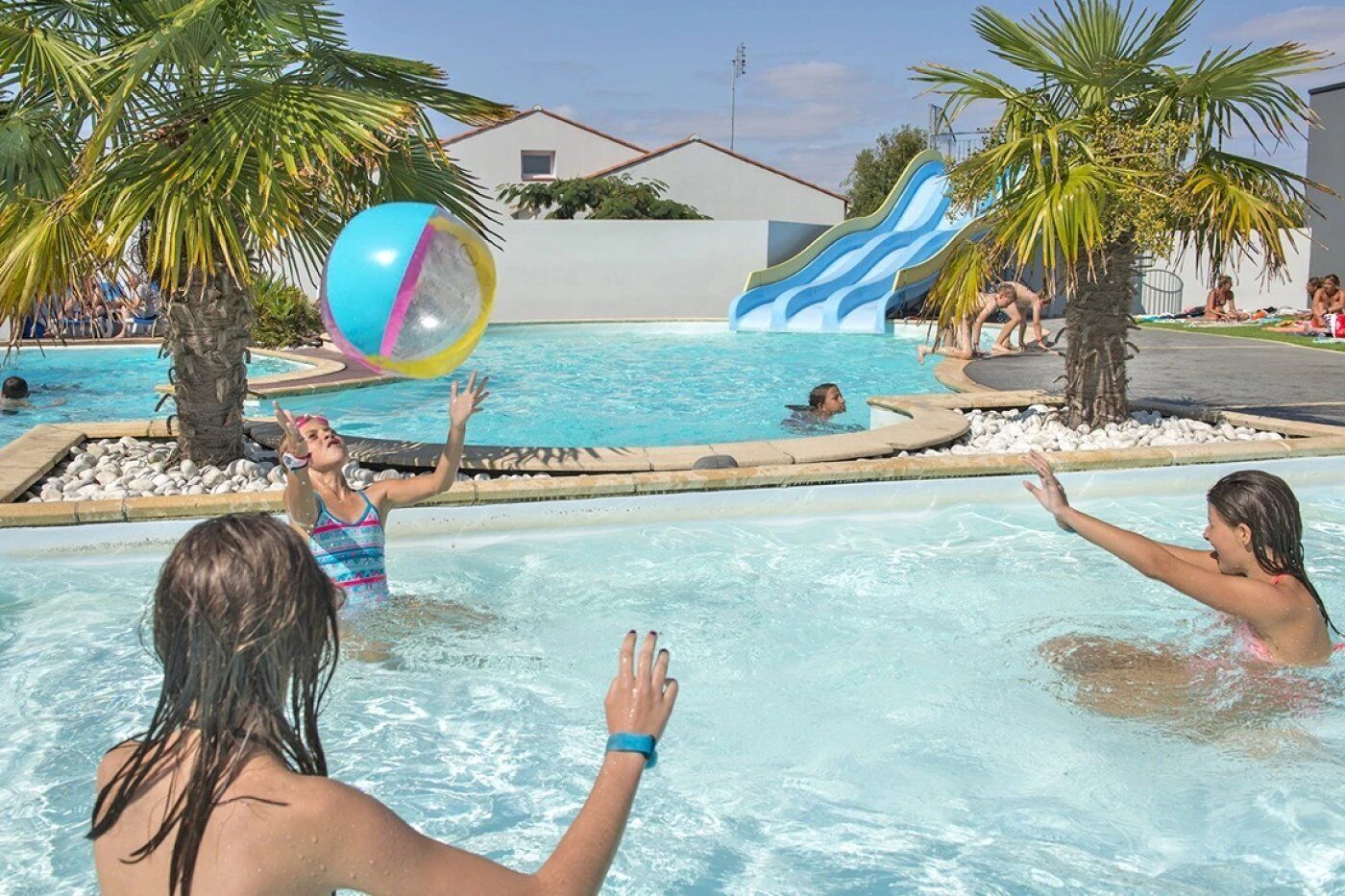 Un espace piscine doté d’un toboggan et bordé de palmiers.