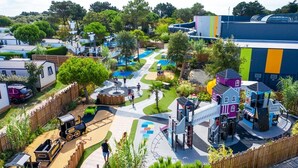 Un parque infantil con diversas estructuras de juego, un tren pequeño y un edificio de fachada colorida.