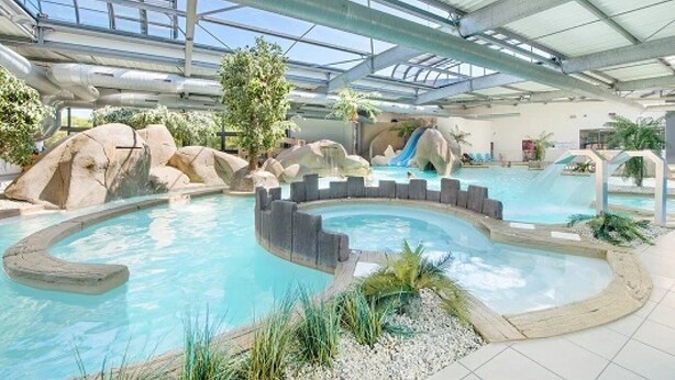 Una piscina interior con tobogán, formaciones rocosas y techo cubierto.