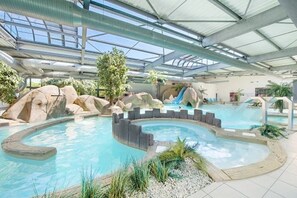 Une piscine intérieure dotée d’un toboggan, de formations rocheuses et d’un toit abrité.