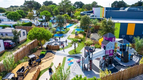 Un terrain de jeux doté de diverses structures ludiques, d’un petit train et d’un bâtiment à la façade colorée.