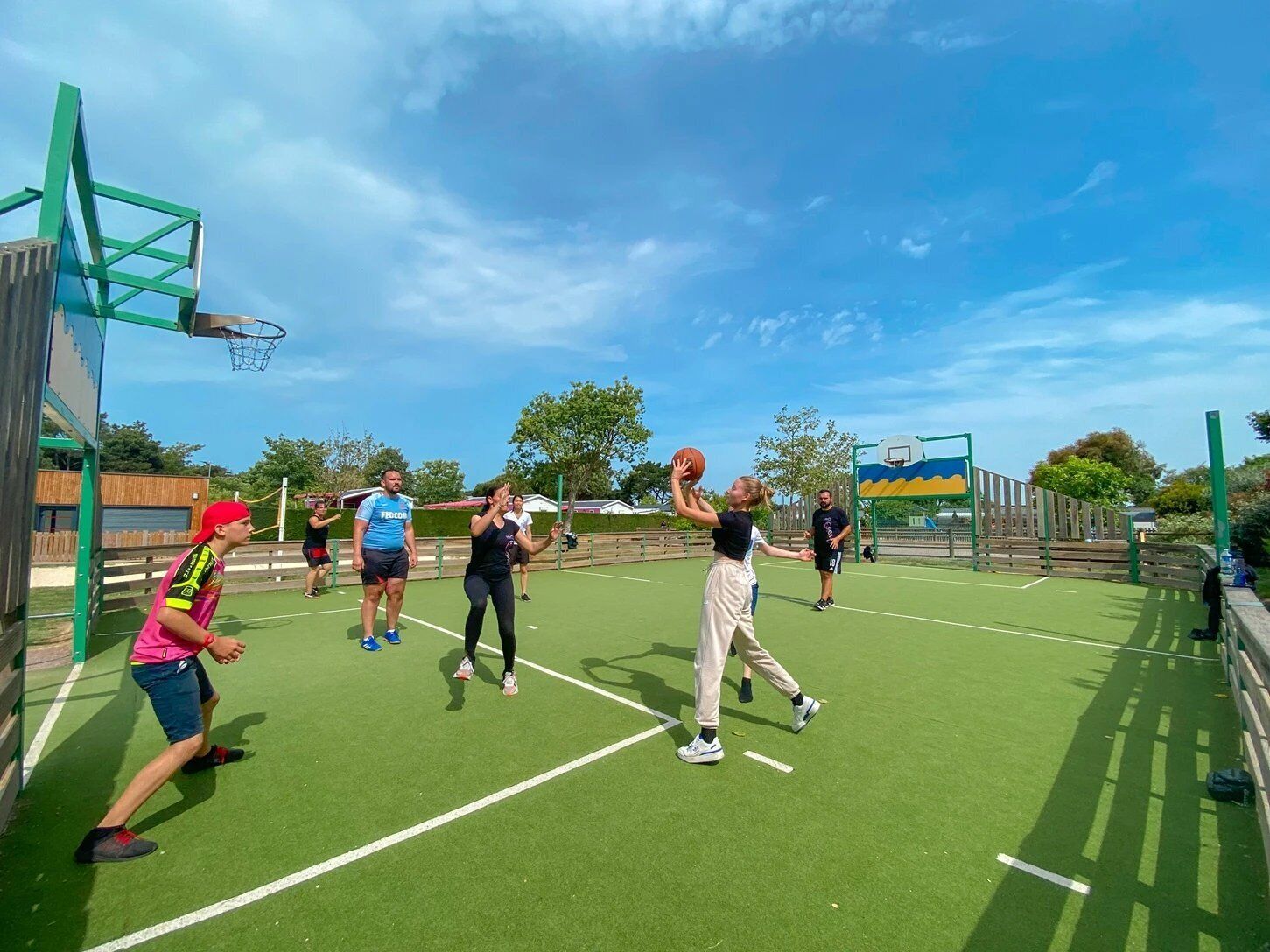 A basketball court with a green surface, a basketball hoop, and a fence.