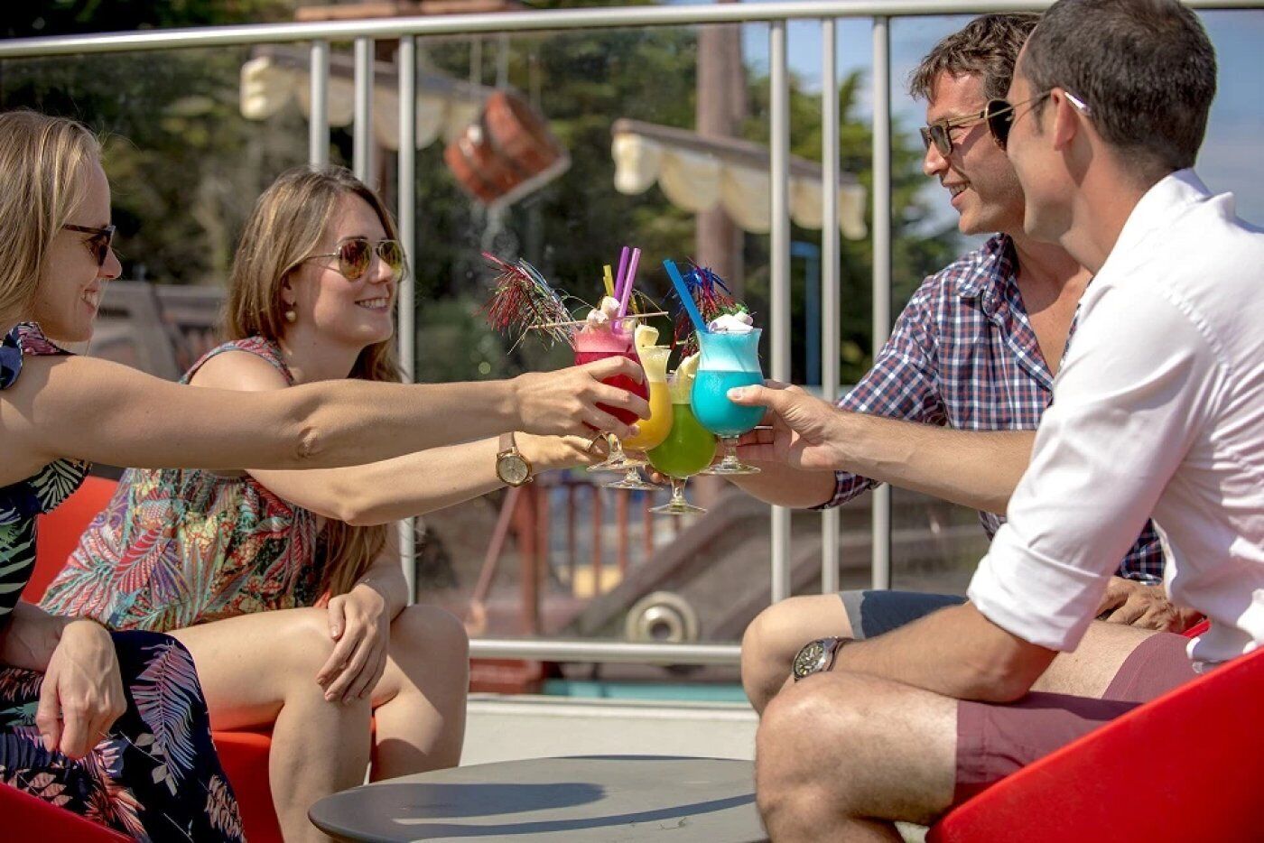A group of people toasting with colorful drinks at a poolside setting.