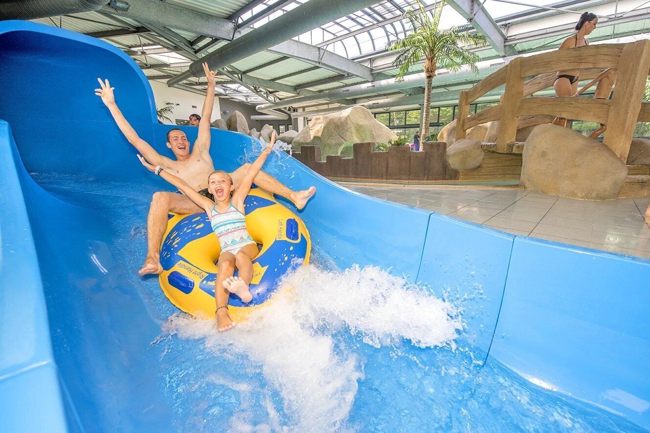 A water slide with a blue and yellow tube, surrounded by a rocky landscape and a glass-enclosed roof.