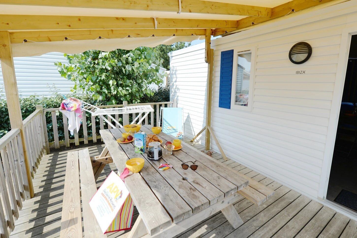 A wooden deck with a picnic table set up, surrounded by a white cabin with blue shutters.