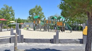 Un patio de juegos con estructuras para escalar y toboganes, rodeado por una valla de madera y árboles.