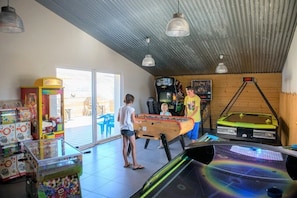 Uma sala de lazer com jogos de fliperama, mesa de pebolim e mesa de pingue-pongue.