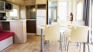 Una cocina compacta con microondas, estufa y refrigerador, un comedor con mesa y sillas, y un sofá rojo.