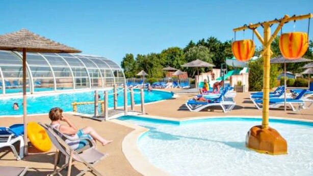 Un área de piscina con sillones de descanso y una zona de estar techada.