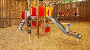 A wooden play structure with a slide and climbing elements, set on a ground covered with wood chips.