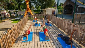 A wooden deck with people performing yoga on blue mats.
