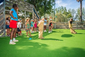 A group of people engaged in an outdoor activity on a green field with a wooden structure in the background.