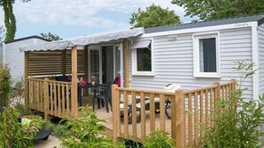 Une maison mobile dotée d’une terrasse en bois, d’un patio couvert et d’un petit espace extérieur aménagé pour s’asseoir.