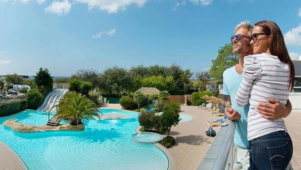 Un espace piscine dans un complexe hôtelier, avec un toboggan aquatique, des chaises longues et des palmiers.