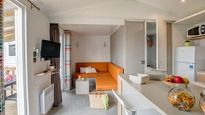 Une chambre d’hôtel compacte comprenant un canapé-lit, un téléviseur à écran plat, un petit coin cuisine avec un four à micro-ondes et un réfrigérateur, ainsi qu’une table à manger avec un saladier de fruits.