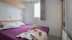 Une chambre à coucher avec un lit, une fenêtre avec des rideaux, une table de chevet et une commode.
