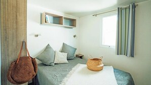 Ein Schlafzimmer mit Bett, Kissen, einer hängenden Tasche, einem kleinen Regal und einem Fenster mit Vorhängen.