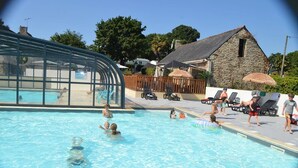 A swimming pool with clear water, surrounded by lounge chairs and umbrellas, and a stone building in the background.