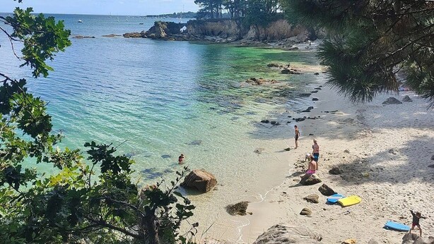 A beach with clear turquoise water, rocky shoreline, and people enjoying the area.