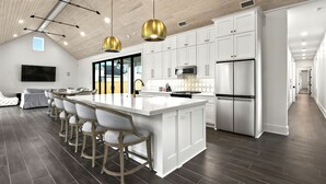 A modern kitchen with white cabinetry, a large island with bar stools, stainless steel appliances, and a wooden ceiling. - The Luxe on Main is an Ultra-Modern, Trendy New Construction in Downtown BSL. (Bay St. Louis)