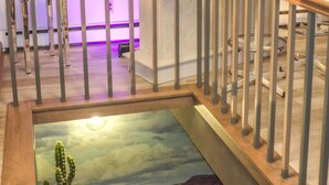 Un escalier avec une rampe en bois, un cactus dans un pot, une photographie encadrée accrochée au mur et un miroir au-dessus d’un coin salon.