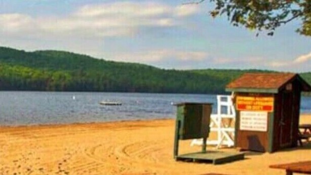 Una playa con un muelle de madera que se adentra en un lago, rodeada de colinas boscosas.