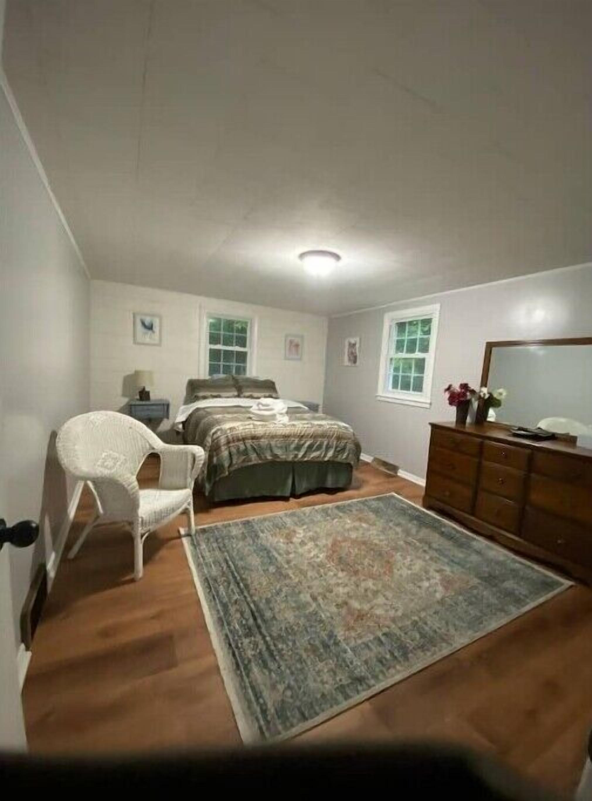 A bedroom with a bed, a chair, a dresser, and a rug.