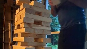 Una persona apila bloques de madera en una habitación con un ventanal y una puerta.