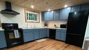 Una cocina moderna con suelo de madera, armarios empotrados, un refrigerador negro y una estufa.