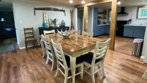 Un comedor con una mesa y sillas de madera, una cocina al fondo y un techo con vigas de madera.