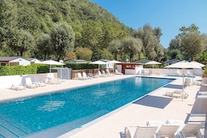 Une piscine entourée de bâtiments et d’arbres, avec des chaises longues et des parasols.