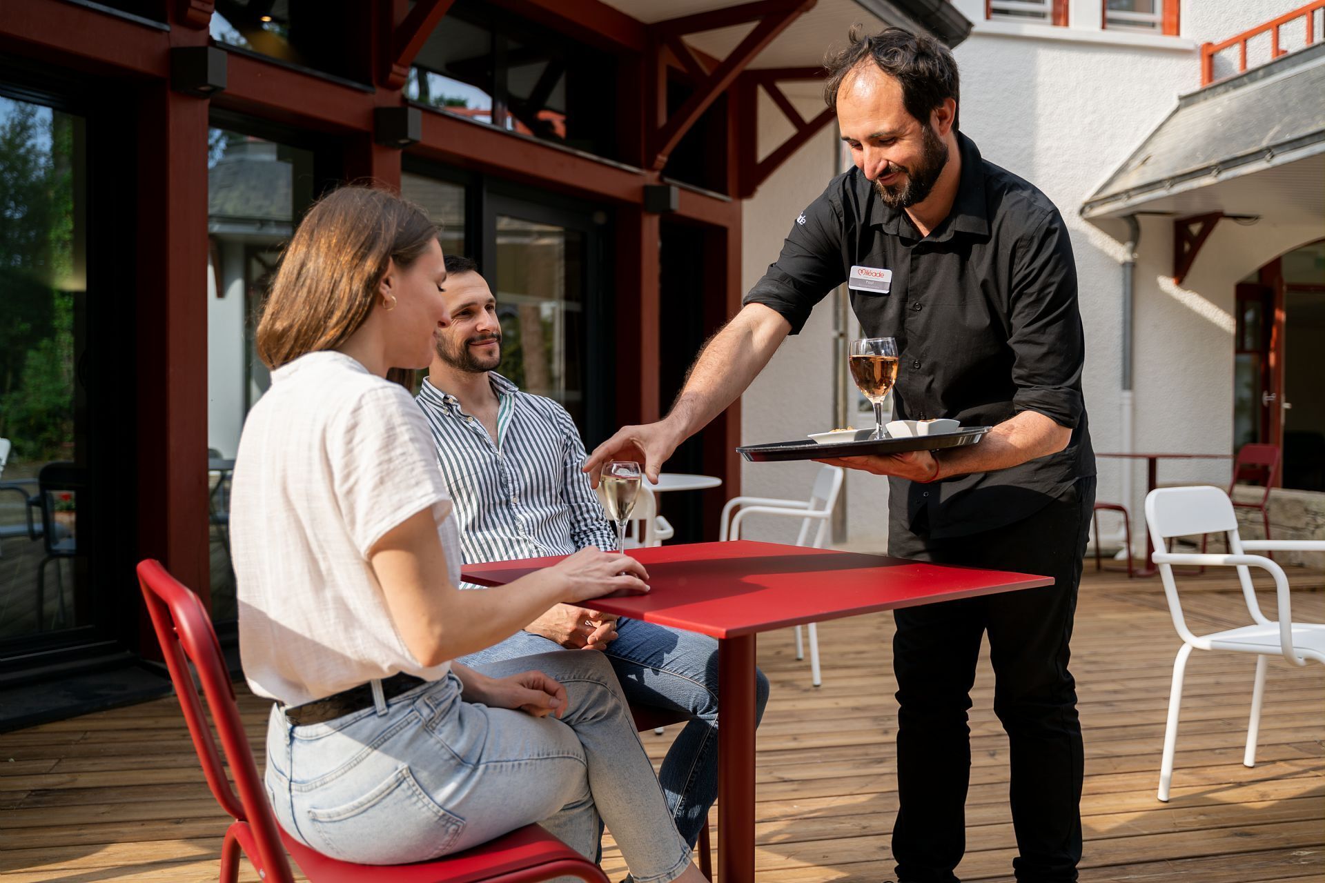 Un camarero sirve una copa de vino a una pareja en una mesa al aire libre.