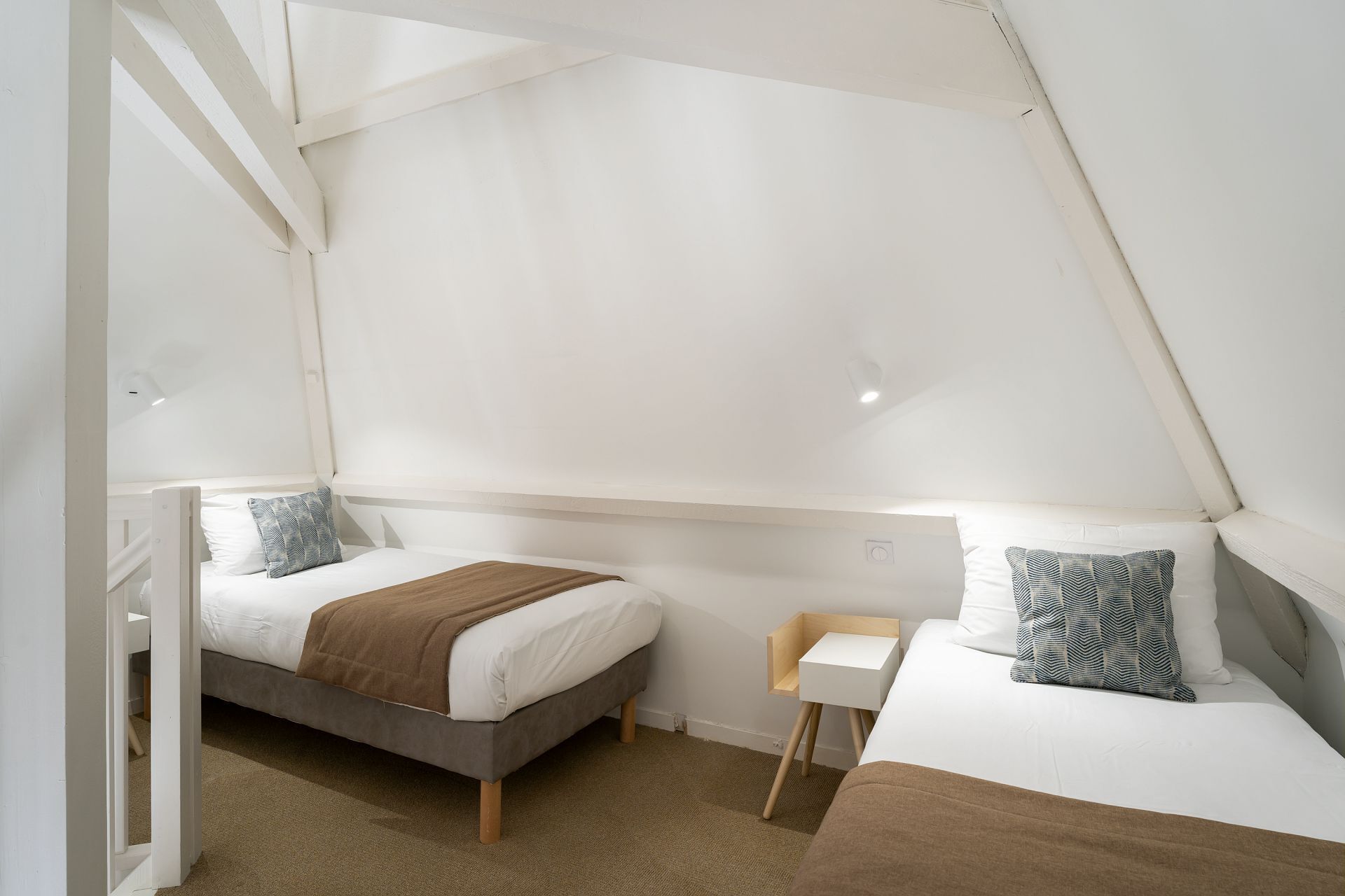 A bedroom with two beds, a small white table, and a slanted ceiling.