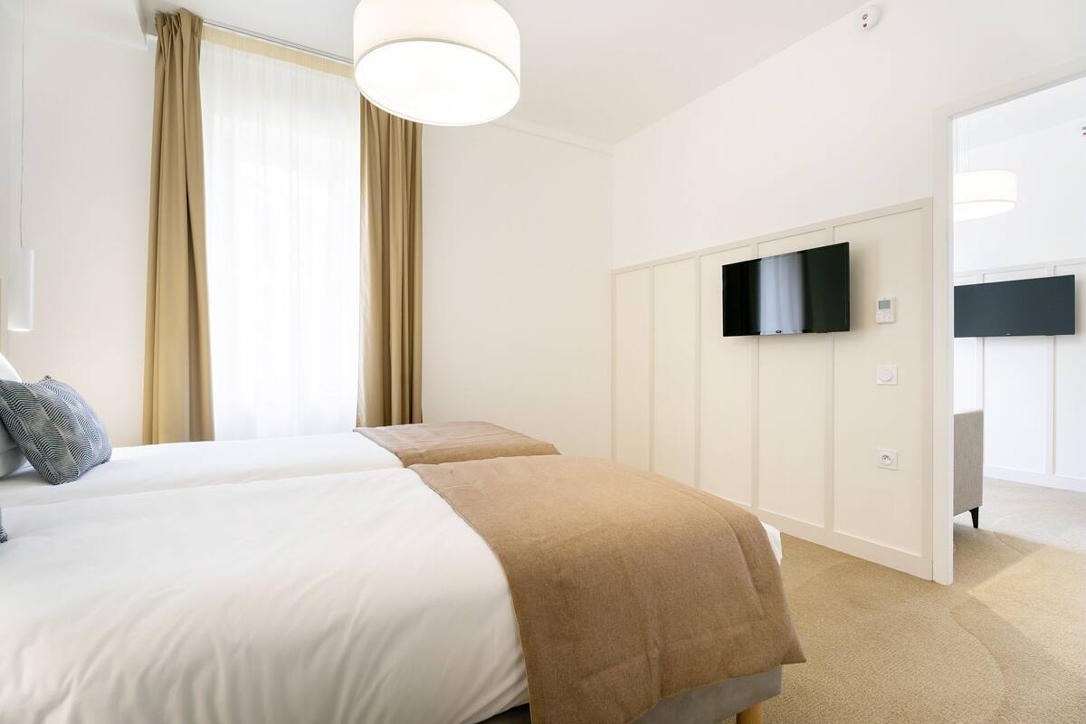 Quarto de hotel com duas camas, televisão de tela plana fixada na parede e um guarda-roupa.