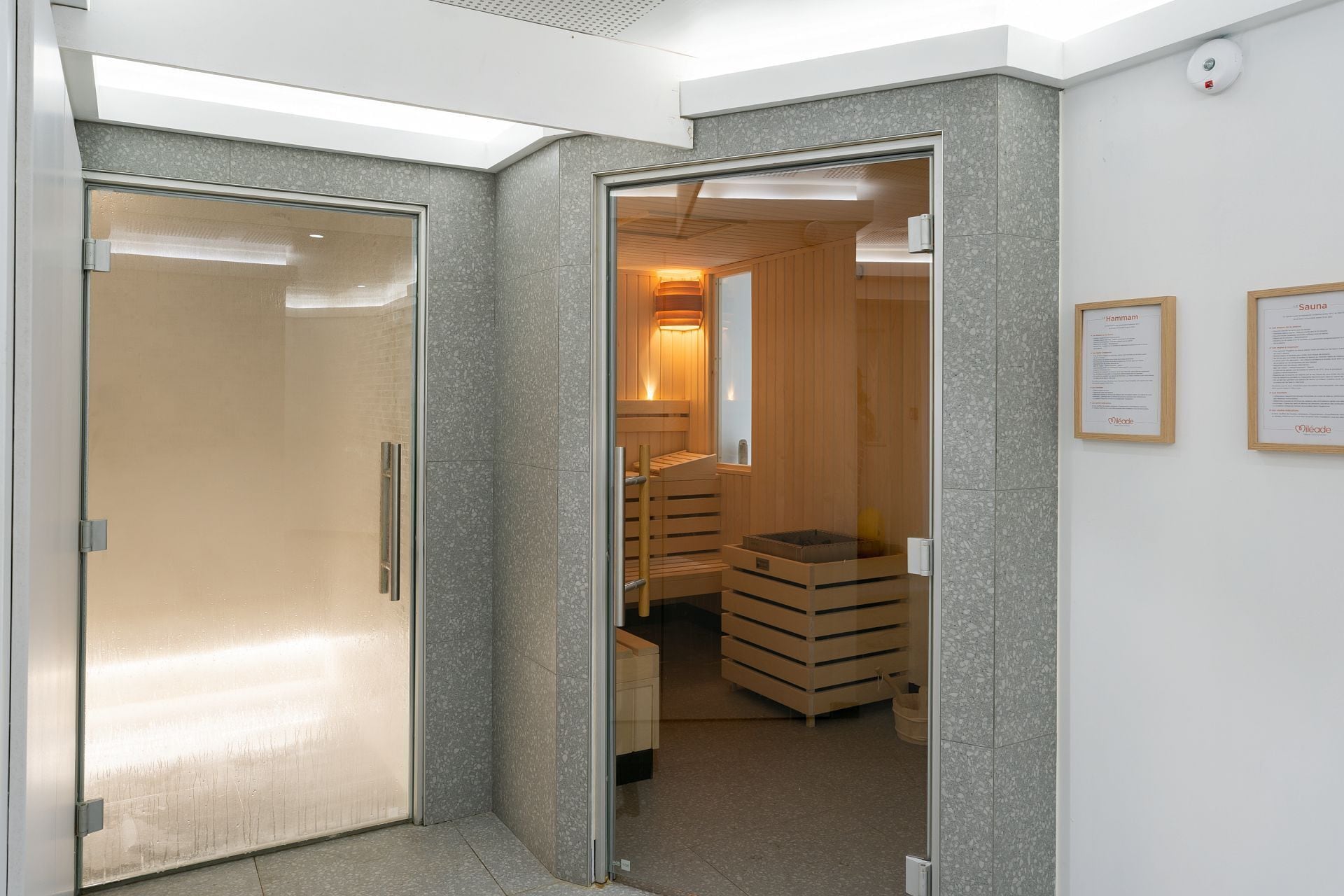 A sauna room with wooden benches and a glass door leading to a hallway.