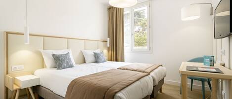 A hotel room with a double bed, a desk with a chair, a television, and a window with curtains.