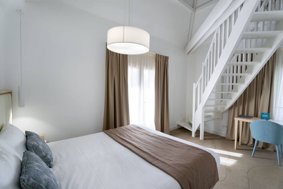 Quarto de hotel moderno com uma cama, uma escrivaninha, uma cadeira e uma escada.