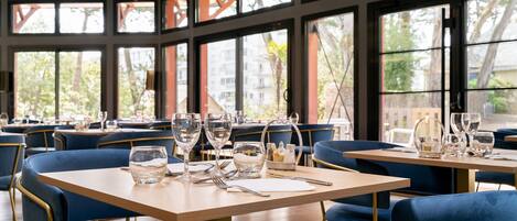 Um restaurante com várias mesas e cadeiras, janelas amplas e vista para o exterior.