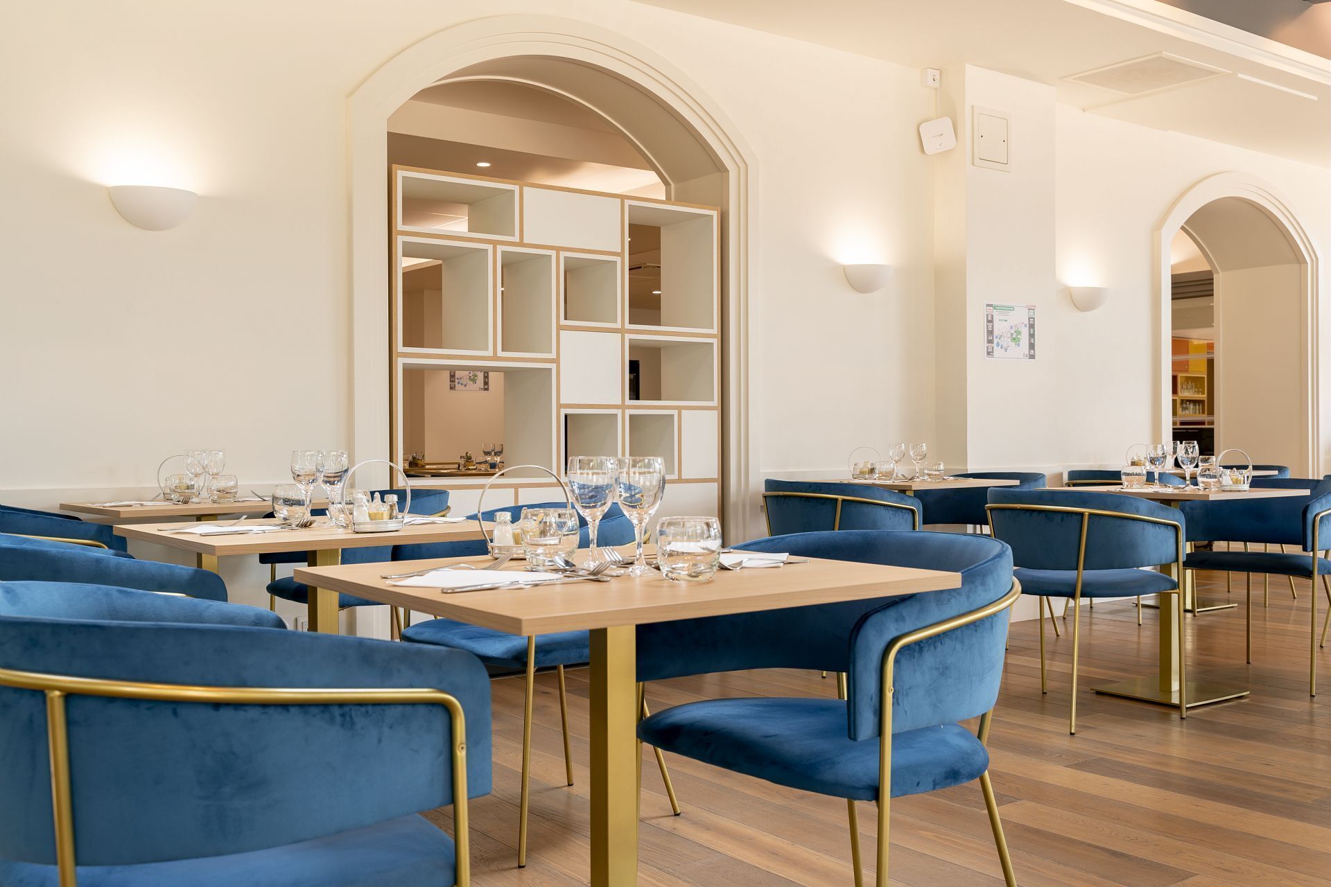 A modern dining area with blue upholstered chairs and wooden tables, featuring an arched ceiling and built-in shelving.